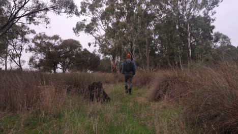 A-fisherman-walks-through-scrub-and-bush-in-the-Wimmera-on-a-dry-creek-bed-with-a-fishing-rod-in-his-backpack