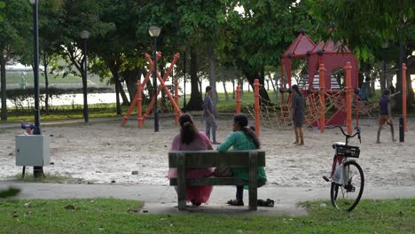 Two-Indian-ladies-talk-at-the-park-overlooking-kids-playground-,-Changi-Beach-Park,-Singapore