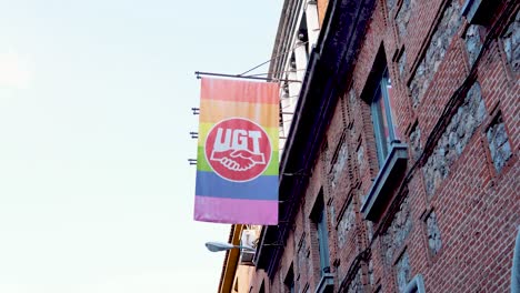 LGTBQ-rainbow-flag-with-supporting-UGT-union-logo-hanging-from-a-brick-building-outdoors-in-Madrid,-Spain