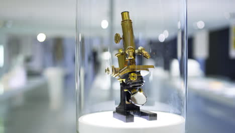 Pan-down-to-an-ancient-microscope-model-made-from-brass,-being-displayed-in-an-optics-museum-showcase