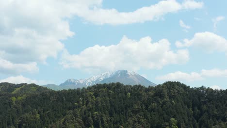 Aerial-reveal-of-Mt-Daisen-rising-over-forest,-Tottori-Japan