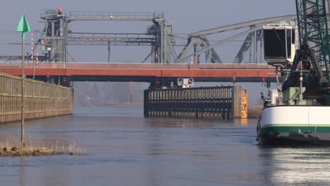 Draw-bridge-corridor-with-dredging-ship-in-front-clearing-the-waterway-of-river-IJssel-for-cargo-ships