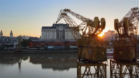 Aerial-dolly-right-shot-of-the-sun-setting-behind-old-port-cranes-in-Puerto-Madero-waterfront,-Buenos-Aires