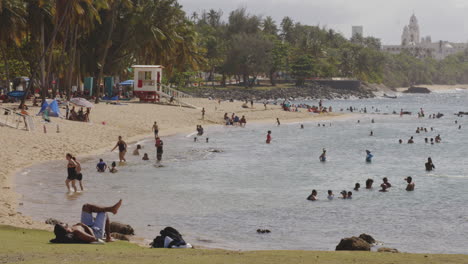 People-enjoying-the-sunshine,-walking-and-swimming-on-the-beach-in-San-Juan,-Puerto-Rico