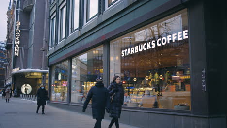 People-walk-by-Stockmann-and-Starbucks-signs-on-Helsinki-street,-slomo