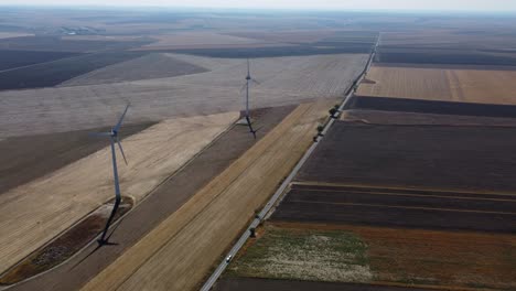 Wind-turbines-in-vast-area-next-to-country-road,-drone-reveal-shot