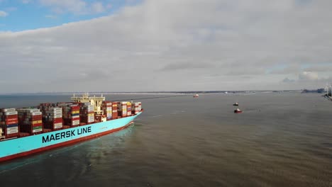 Giant-containervessel-loaded-with-containers-on-deck-entering-the-Port-of-Rotterdam-with-two-small-tug-boats-are-waiting-to-assist-the-vessel-to-her-berth-on-a-partly-cloudy-calm-day