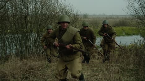 Soldados-Corriendo-En-Un-Campo-Pantanoso-Con-Rifles-De-La-Segunda-Guerra-Mundial-Y-Un-Soldado-Herido-Tocando-Su-Herida-Sangrienta