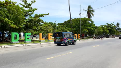 A-colourful-blue-microlet-public-transport-bus-on-a-busy-street-with-popular-landmark-in-the-capital-city-Dili,-Timor-Leste,-Southeast-Asia