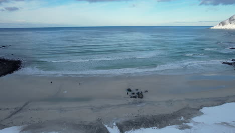 Beautiful-sandy-beach-in-Northern-Norway-partly-covered-in-snow,-Flakstad-Beach-Lofoten,-Aerial-view,-sliding-shot