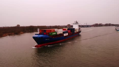 Aerial-View-Of-Forward-Bow-Of-JSP-Carla-Transporting-Cargo-Containers-On-River-On-Cloudy-Day