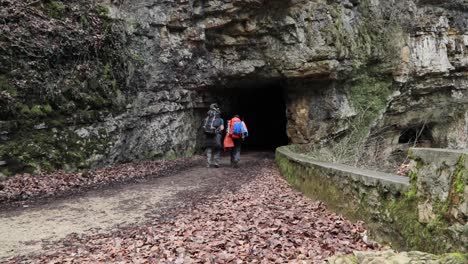 Two-backpackers-hiking-into-a-tunnel-in-a-mountain-outdoors