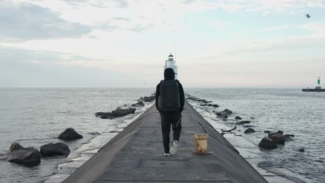 Man-with-hoodie-walking-towards-the-lighthouse-with-book-bog