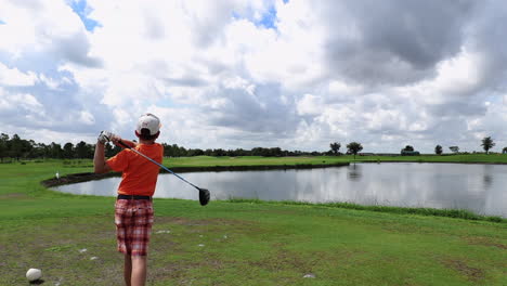 A-young-boy-runs-up-and-hits-a-golf-ball-over-a-lake-in-slow-motion