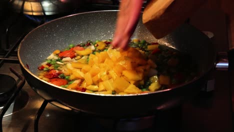 Pouring-freshly-chopped-yellow-bell-pepper-on-top-of-vegetables-in-hot-frying-pan-from-a-wooden-cutting-board