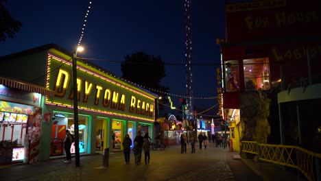 Busy-Business-Street-Featuring-A-Popular-Merchandise-Store-With-People-Walking-During-The-Night-In-Vienna-Prater---Steady-Shot