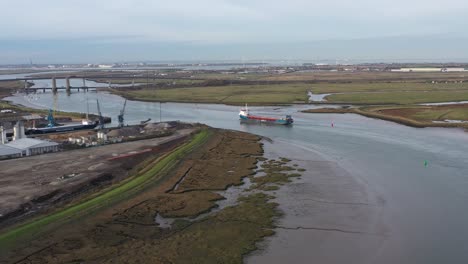 Wide-aerial-view-of-Ridham-Dock-in-Kemsley,-UK-with-a-ship-sailing-along-the-Swale
