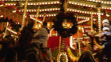 Close-up-view-of-spinning-carousel-at-night-filled-with-riders-and-decorated-for-Christmas-holiday-season