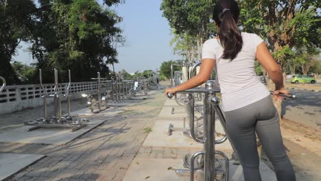 A-woman-on-a-swinging-equipment-in-an-outdoor-gym-in-Thailand,-toning-her-hips-and-waist---Wide-shot