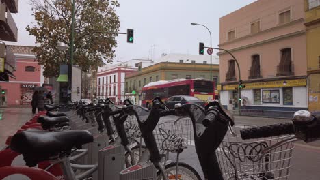 Bus-and-cars-driving-past-row-of-rental-bikes-in-rainy-city-panorama