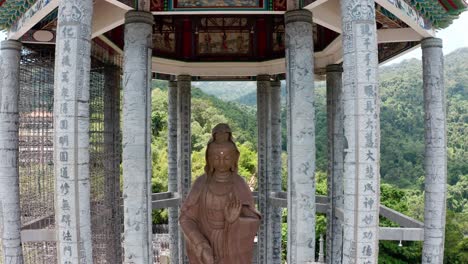 Kuan-Yin-Goddess-of-Mercy-monumental-statue-located-in-Kek-Lok-Si-Buddhist-temple-pavilion,-Aerial-drone-pedestal-down-medium-shot
