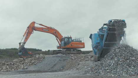 Stone-spills-from-rock-conveyor-in-quarry-while-digger-picks-up-stone-background