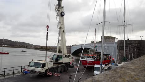 Heavy-hydraulic-crane-vehicle-lifting-fishing-boat-on-Conwy-Wales-harbour-dolly-left-back
