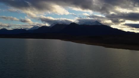 Dezdeash-lake-at-sunset-over-mountain-range,-panning-drone-shot