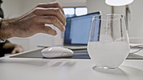 White-person-hand-taking-glass-of-water-with-effervescent-tablet-while-working