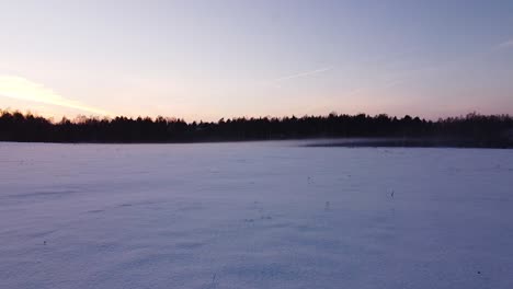 Wunderschöner-Tiefflug-über-Schneebedecktem,-Frostigem-Feld,-Neblige,-Neblige-Abendlandschaft-Nach-Sonnenuntergang,-Weitwinkel-Drohnenaufnahme,-Die-Sich-Tief-über-Den-Boden-Bewegt