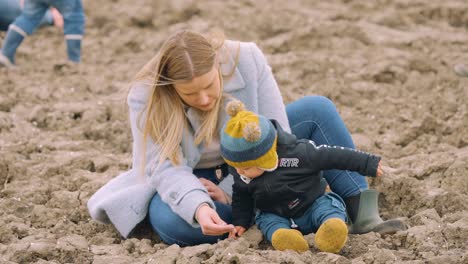 Young-mother-and-son-in-winter-clothes-playing-on-the-beach-together-in-slow-motion