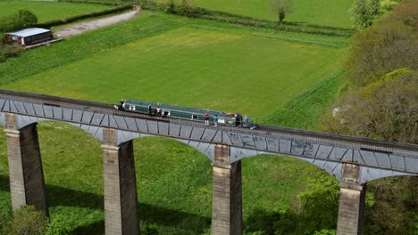 Aerial-view-following-narrow-boat-on-Trevor-basin-Pontcysyllte-aqueduct-crossing-in-Welsh-valley-countryside-tracking-rising-left