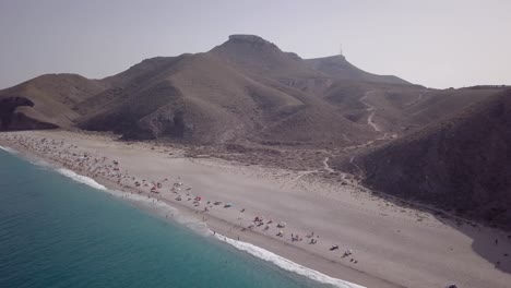 Summertime-holiday-view-of-Playa-Muertos-beach-in-Spain,-tourists-enjoying-vacation,-aerial-drone-flying-above-sea,-sideway,-daytime