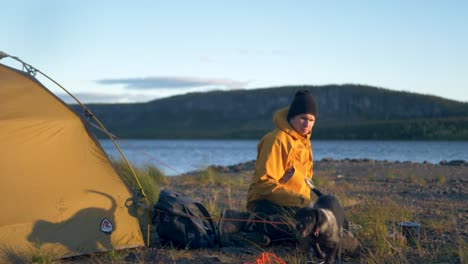 Camping-Enthusiast-Genießt-Den-Schwedischen-Sonnenuntergang-Mit-Seinem-Hund-–-Bodennahe-Weitwinkelaufnahme-In-Mittlerer-Zeitlupe