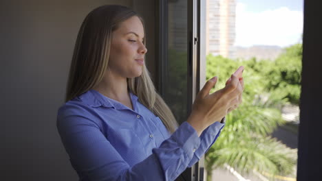 Happy-woman-taking-selfie-photo-with-cellphone-by-window-at-home