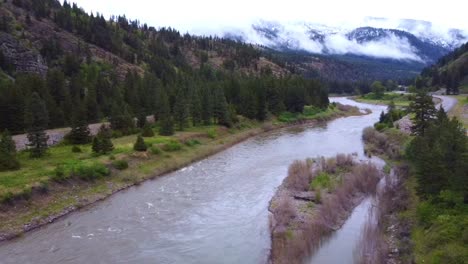 Slow-moving-drone-shot-of-river-with-freshly-snow-capped-mountains-in-the-background