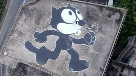 Hong-Kong-locals-on-an-abandoned-industrial-rooftop-decorated-with-a-large-graffiti-of-Felix-the-Cat,-Aerial-view
