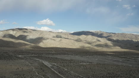 Desert-mountains-and-cloud-shadows-with-highway-in-distance