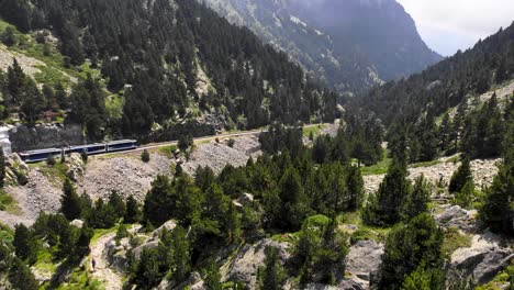 Aerial:-rack-railway-running-along-a-green-valley-and-some-hikers-in-a-path