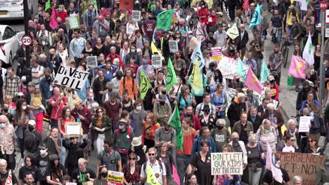 An-overheard-view-of-hundreds-of-people,-many-in-face-masks,-march-on-with-placards-and-flags-on-an-Extinction-Rebellion-climate-change-protest