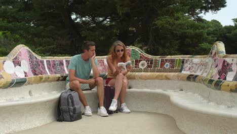 A-young-couple-sitting-on-the-famous-mosaic-ceramic-benches-of-Park-Guell-and-discussing-their-itinerary