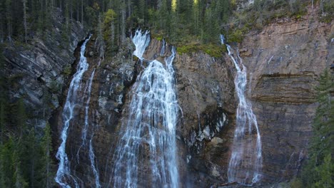Drone-flying-backwards-revealing-a-huge-waterfall-surrounded-by-woods-in-Canmore,-Alberta