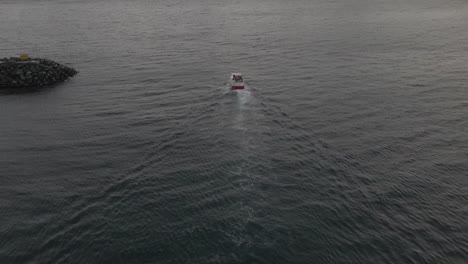 Commercial-fishing-vessel-exits-safety-of-harbour-into-the-open-Arctic-ocean,-drone