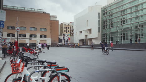 Barcelona---Plaça-Dels-Àngels,-Fuera-Del-Museo-De-Arte-Contemporáneo-Con-Turistas,-Skaters-Y-Bicicletas