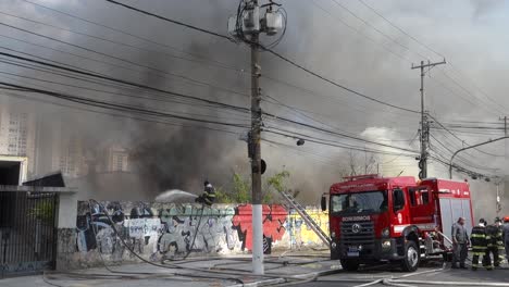 Equipo-De-Bomberos-Y-Camión-De-Bomberos-Combatiendo-Un-Gran-Incendio-Con-Humo-Negro-Que-Quemó-Un-Cobertizo-Mecánico-En-Sao-Paulo,-Brasil