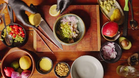 Preparation-of-Ceviche---table-top-view-of-a-profession-chef-cutting-the-lemon-into-half-and-squeezing-it-into-a-bowl-of-fresh-ingredients,-giving-the-dish-some-citrusy,-cooking-scene-concept