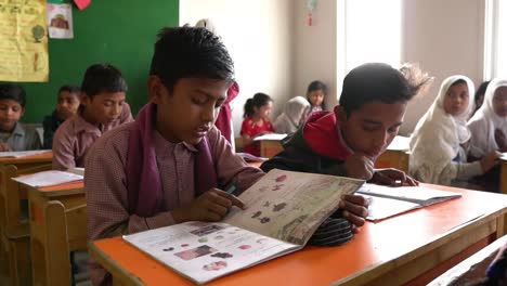 Two-Young-Muslim-School-Boys-Reading-Book-At-Desk-In-Classroom-In-Karachi,-Pakistan