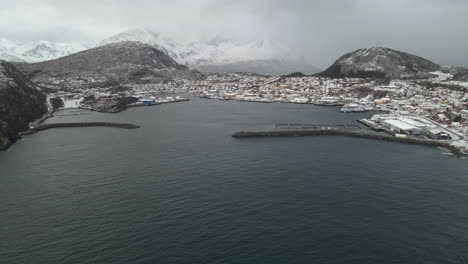 Aerial-approach---harbour-at-Skjervoy-village,-nestled-under-snowy-mountains,-Norway