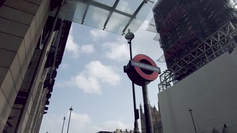 Shot-of-a-London-Underground-sign-at-Westminster-station,-across-the-street-a-closed-construction-site-as-the-iconic-Big-Ben-undergoes-a-restoration-project,-Westminster,-London-England