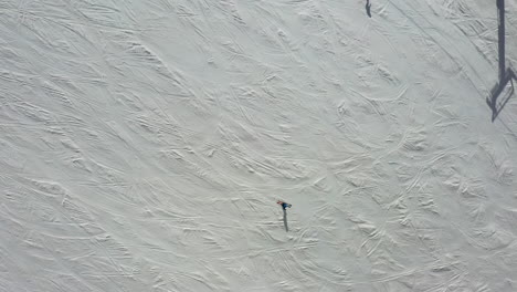 People-enjoy-winter-while-skiing-down-snowy-slopes,-aerial-top-down-view